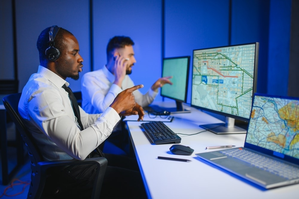 Two logistics dispatchers wearing headsets working on computers with navigation maps in a modern control center.