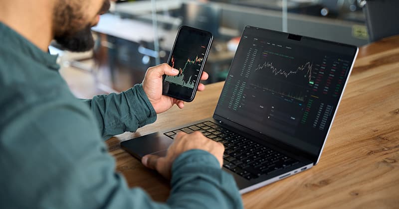 Man looking at stock market on laptop and smartphone