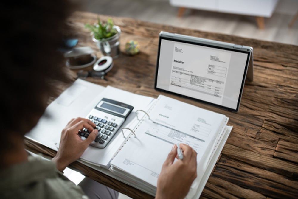 a person reviewing financial documents and calculating an invoice at a wooden desk