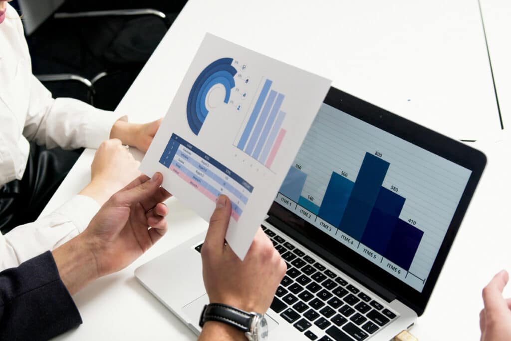Person reviewing performance data from a printed report alongside field workforce management software on a laptop.