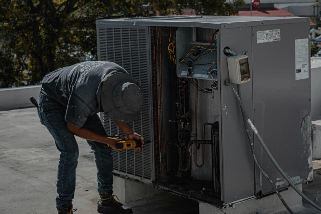 Certified electrician servicing an outdoor HVAC unit while inspecting wiring and system components.
