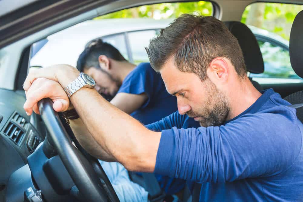 • A bored and tired man resting his head on a car steering wheel while stuck in heavy traffic.